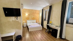Een hotelkamer met een bed, bureau, televisie en een raam met gordijnen.