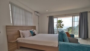 A bedroom with a large bed, a nightstand, a window with curtains, and a view of the outdoors. - Cozy 1-bedroom studio in beautiful Anse Royale with AC (Anse Royale)