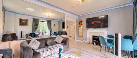 The grey velvet sofa faces the wall-mounted TV above the fireplace