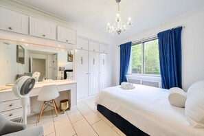 Ein Schlafzimmer mit einem großen Bett, einem Schreibtisch mit Stuhl, einem Spiegel und einem Fenster mit Vorhängen.
