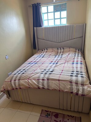 Ein Schlafzimmer mit Bett, einem Fenster mit Vorhängen, einem Heizkörper und einer Steckdose.