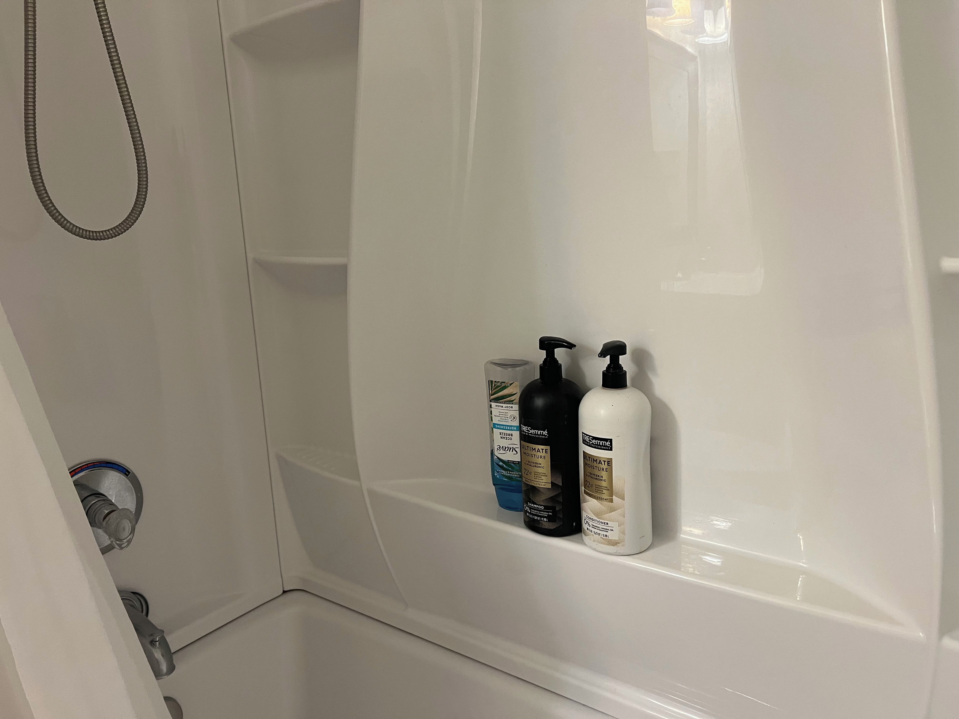 Ein Badezimmer mit Dusche, Handtuchhalter und drei Flaschen Shampoo und Conditioner.
