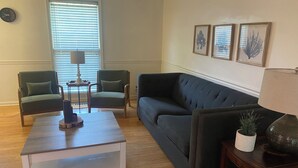 Ein Wohnzimmer mit einer Couch, zwei Sesseln, einem Couchtisch, einer Lampe und gerahmten Kunstwerken an der Wand.