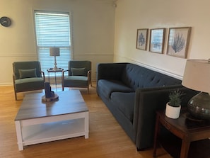 A living room with a sofa, two armchairs, a coffee table, a lamp, and framed artwork on the wall.