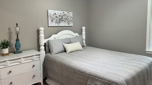 Ein Schlafzimmer mit Bett, Nachttisch, Lampe, einem Gemälde und einem Fenster.