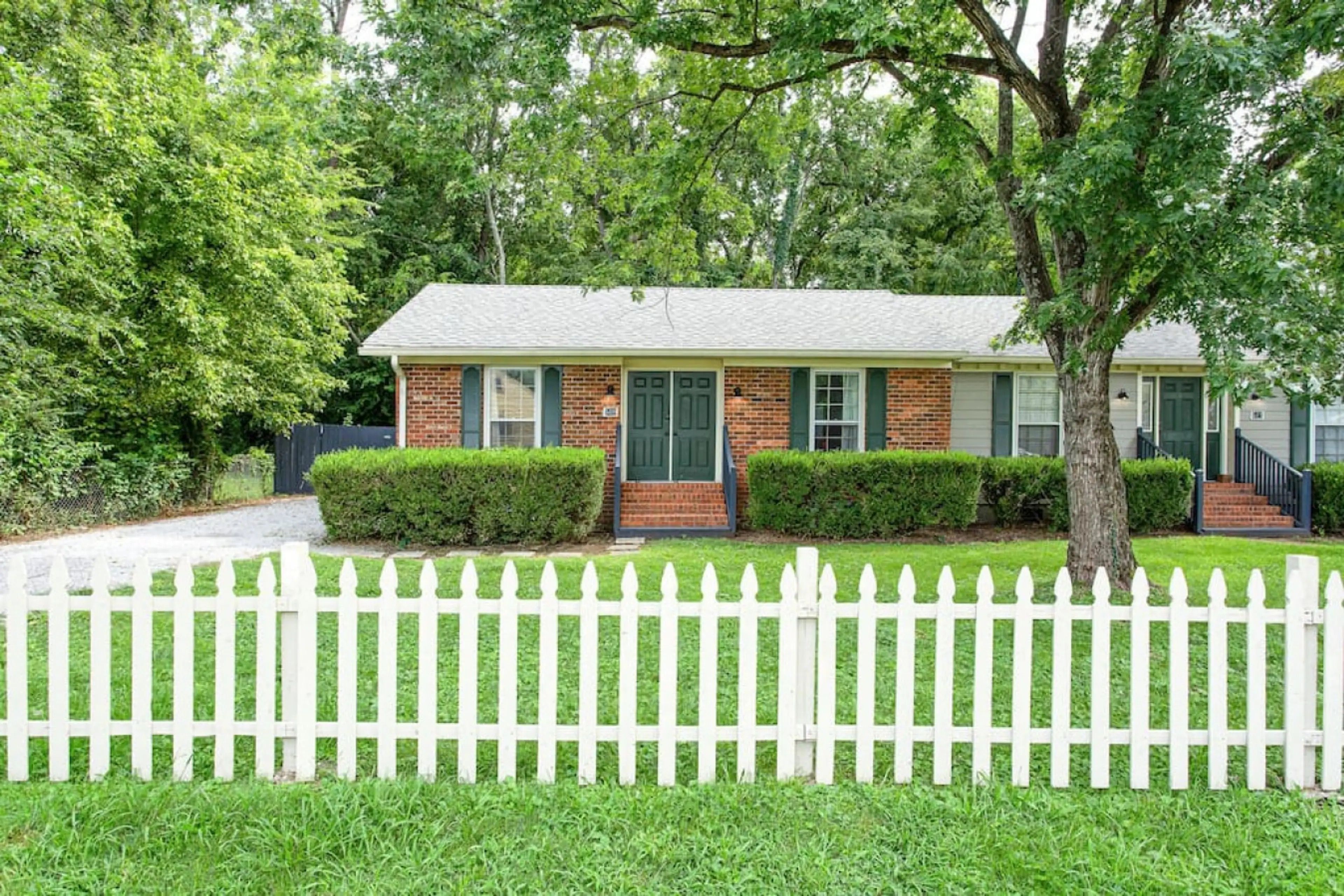 A single-story brick house with a white picket fence, a front door, and a small front yard.