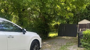 Ein weißes Auto parkt auf einer Schotterauffahrt in einer Wohngegend, mit einem Holzzaun und Grünpflanzen im Hintergrund.