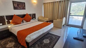 A hotel room with a bed, two chairs, a desk, a ceiling fan, and a large window. - Misty Meadows Resort (Solan)
