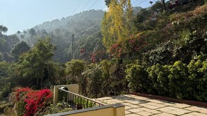 A residential area with a staircase leading to a balcony overlooking a lush garden and a forested hillside. - Misty Meadows Resort (Solan)