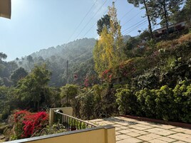 A residential area with a staircase leading to a balcony overlooking a lush garden and a forested hillside.