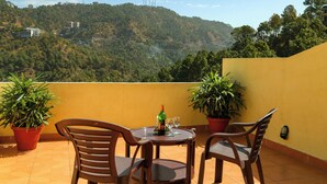 A terrace with a table, chairs, potted plants, and a bottle of wine. - Misty Meadows Resort (Solan)