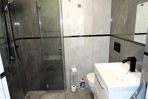 Un baño con cabina de ducha de vidrio, inodoro y lavabo con espejo.
