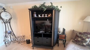 A room with a black entertainment unit, a clock, a bed with patterned pillows, and a lamp. - 1200-505 Standard Plus (Siesta Key)
