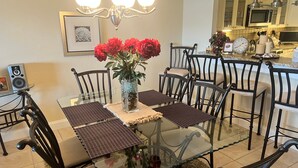 A dining area with a glass table, black chairs, and a vase with red flowers. - 1200-505 Standard Plus (Siesta Key)