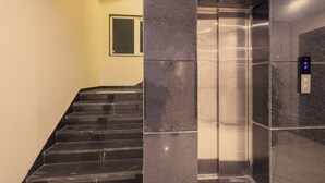 A staircase with a digital elevator control panel and a window in the background. - Hotel Meritel Grande (Indore)
