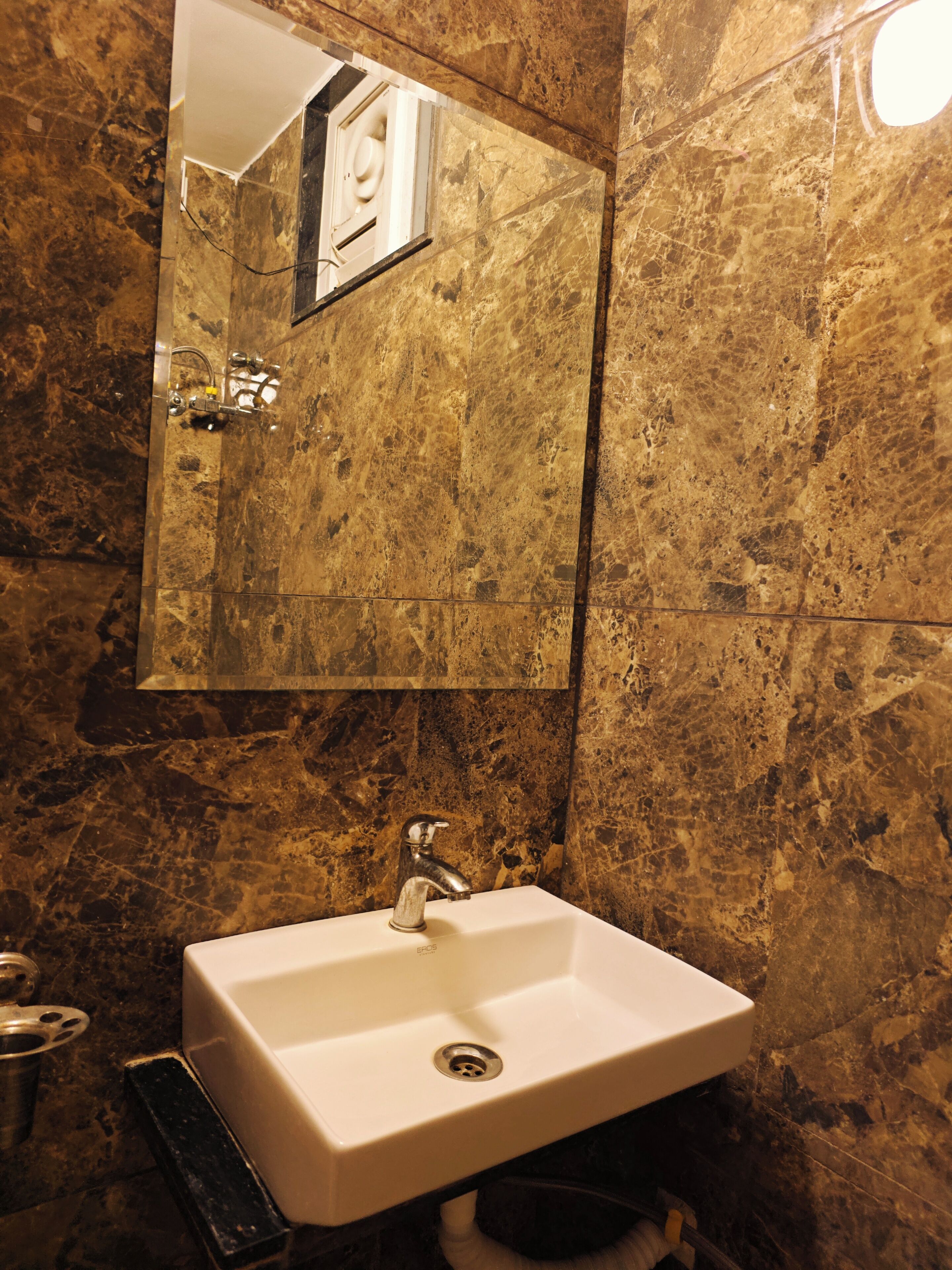 A bathroom with a marble wall, a sink, and a mirror.