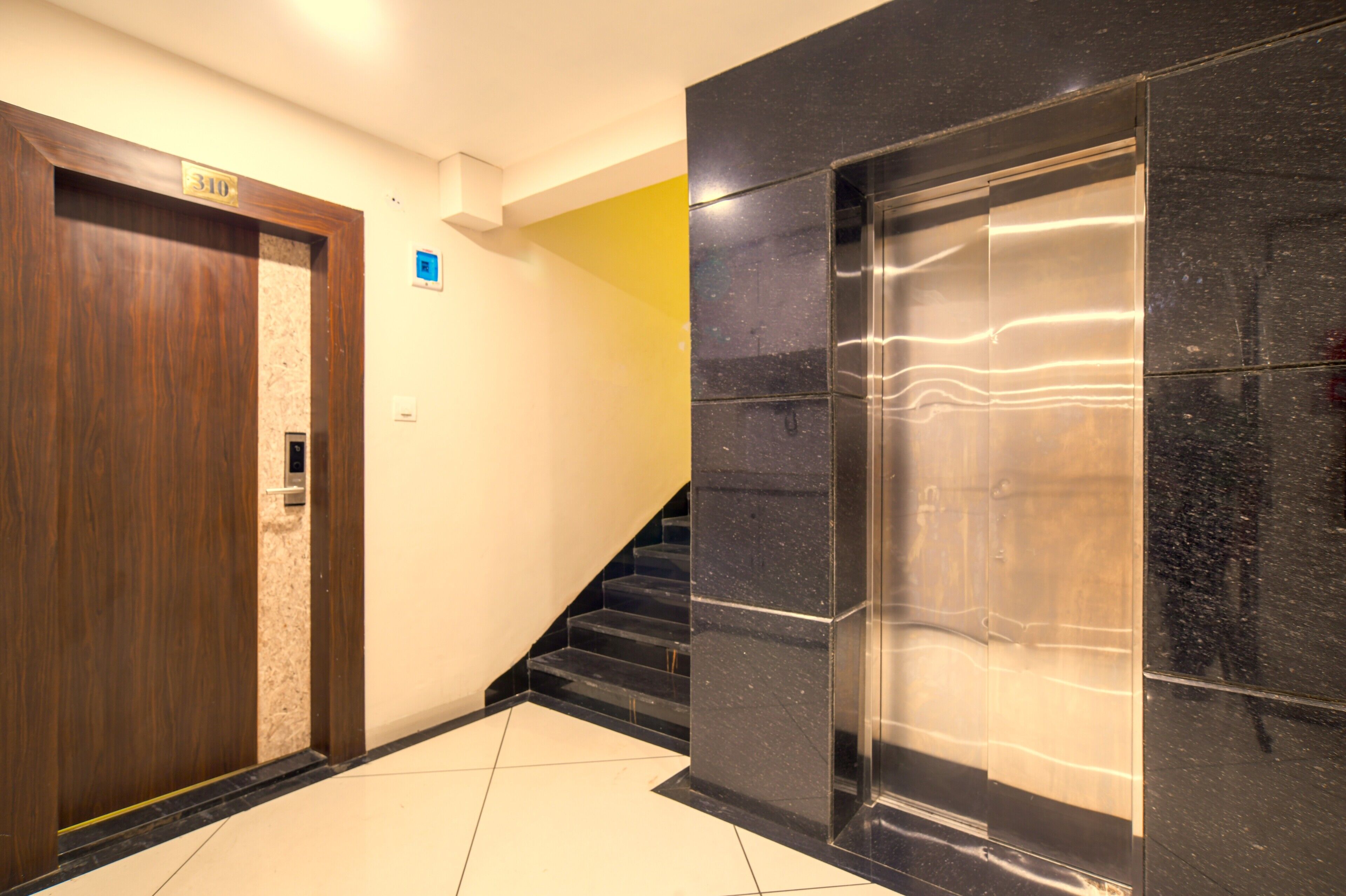 A hotel lobby with a wooden door marked '310', a staircase, and a modern elevator.