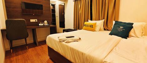 A hotel room with a bed, a desk, a chair, an air conditioner, and curtains.