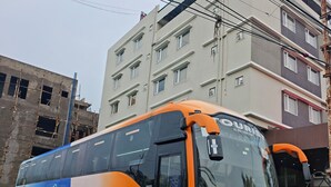 A large, modern bus parked on a dirt road with a building in the background. - Hotel Meritel Grande (Indore)