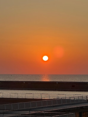 Ein Sonnenuntergang über ruhigem Meer mit einer Brücke im Vordergrund.
