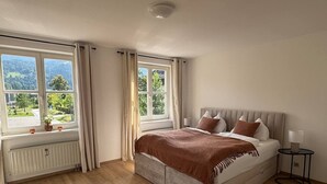 A bedroom with a large bed, a window with curtains, a radiator, and a small table with a lamp. - Faraway Homes Studio Mautern #8 (Mautern in Steiermark)