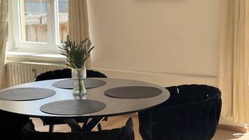 A dining area with a round table, black chairs, a vase with plants, and a large abstract painting on the wall.