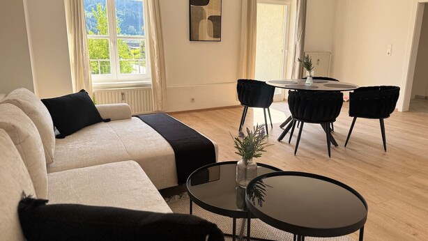A modern living room with a sofa, a round coffee table, and a dining area with chairs. - Faraway Homes Studio Mautern #8 (Mautern in Steiermark)