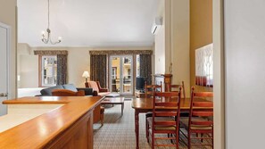Ein Hotelzimmer mit einer Holztrennwand, einer Couch, einem Esstisch mit Stühlen, einem Fernseher und einer Chandelier.