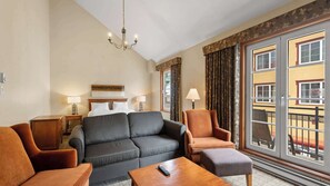 Ein Hotelzimmer mit Sofa, Sesseln, Couchtisch, einer Deckenleuchte, einem Bett und einem Balkon mit Aussicht.