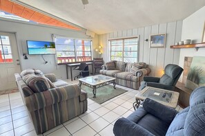 Ein Wohnzimmer mit einer Couch, Sesseln, einem Couchtisch, einem Fernseher und einem Schreibtisch.