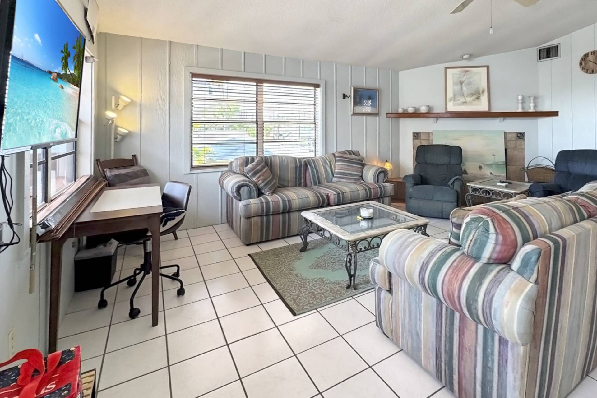 A living room with striped sofas, a coffee table, a desk, and a TV.