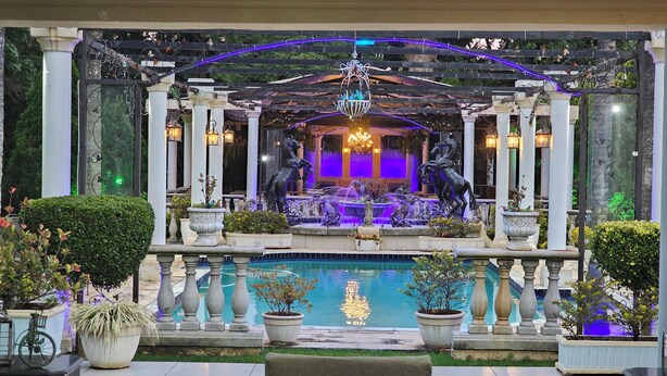 Ein Brunnen mit Statuen, ein Teich und eine Pergola mit Beleuchtung.