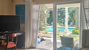 Ein Wohnzimmer mit Fernseher, Glastisch, Sofa und Blick auf Pool und Garten.
