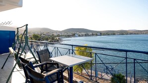 A balcony with a table and chairs overlooking a body of water and a distant town. - Blue Hotel Salamina (Salamis)