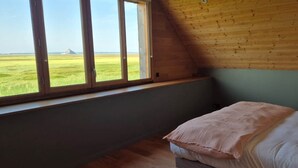 Un dormitorio con un ventanal grande, una cama con almohadas y vistas a un campo.