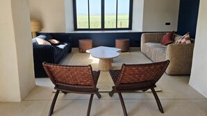 Un salón con dos sofás, una mesa de centro y vistas a un campo a través de amplios ventanales.