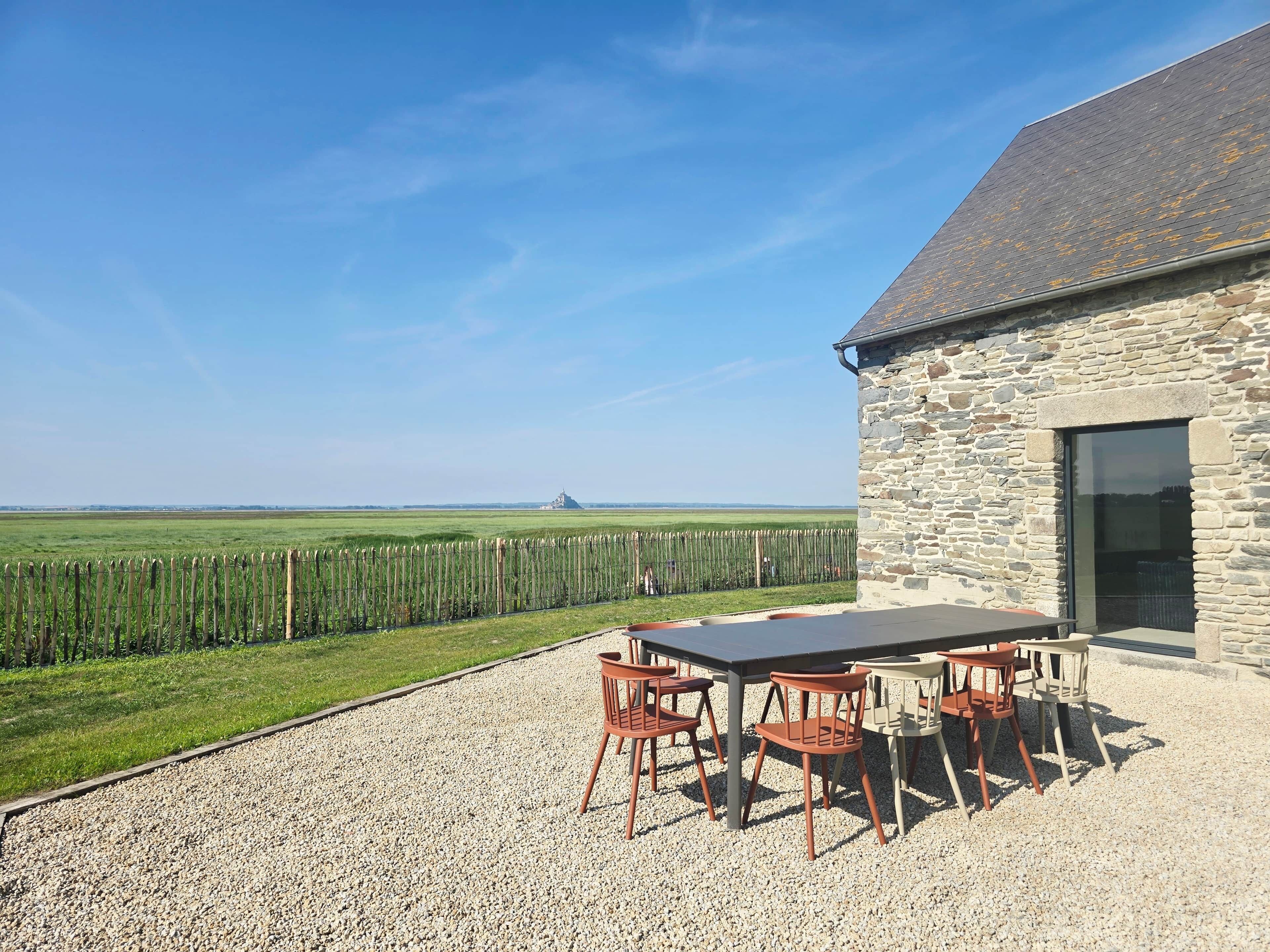 A stone building with a gravel patio, outdoor seating, and a view of a green field.