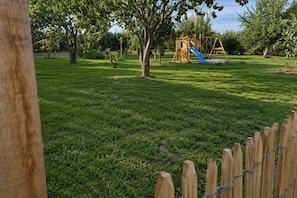 A grassy park area with a wooden play structure and a blue slide. - Gîte Mer - Outdoor Spa (Genêts)