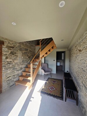 A staircase with wooden steps and a metal railing, leading to a room with a stone wall and a chair. - Gîte Terre - Indoor swimming pool (Genêts)
