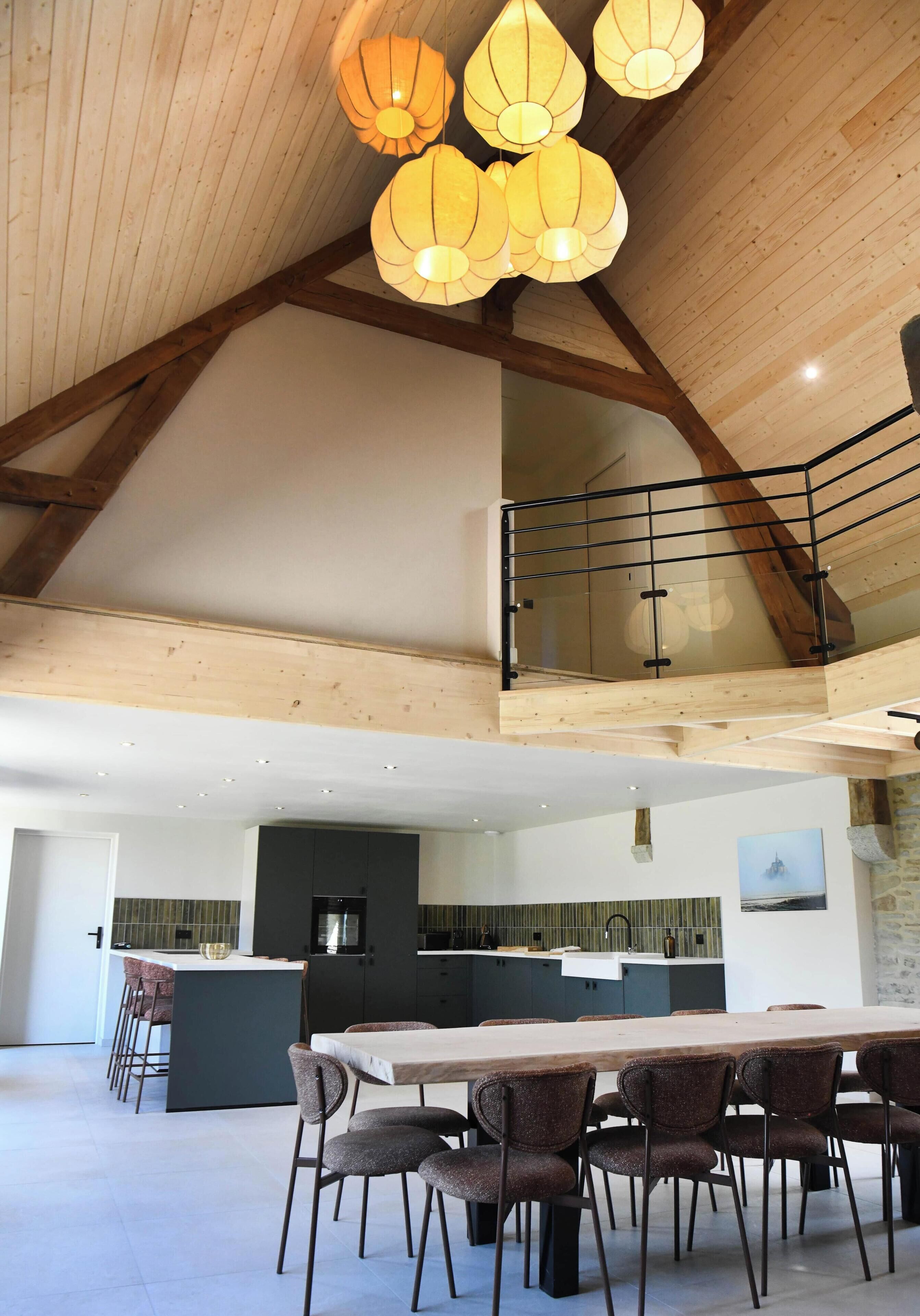 A spacious dining area with a high ceiling and wooden beams, a kitchen with modern appliances, and a staircase leading to an upper level.