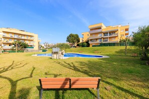 Un espacio verde con una piscina, bancos y edificios de apartamentos al fondo.