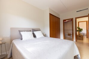Quarto com cama, mesa de cabeceira, luminária e vista para um banheiro adjacente.