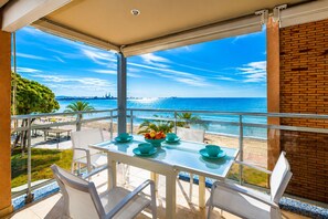 En balkon med et glasbord og stole, med udsigt over en strand og havet.