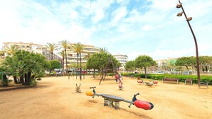 Une aire de jeux avec des balançoires, une bascule et un toboggan.