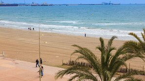 Une plage avec une jetée en arrière-plan, des palmiers et un ciel dégagé.