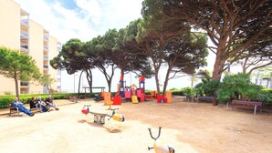 Un espace de jeux avec des balançoires et un toboggan, des bancs et des arbres, le tout aménagé en plein air.