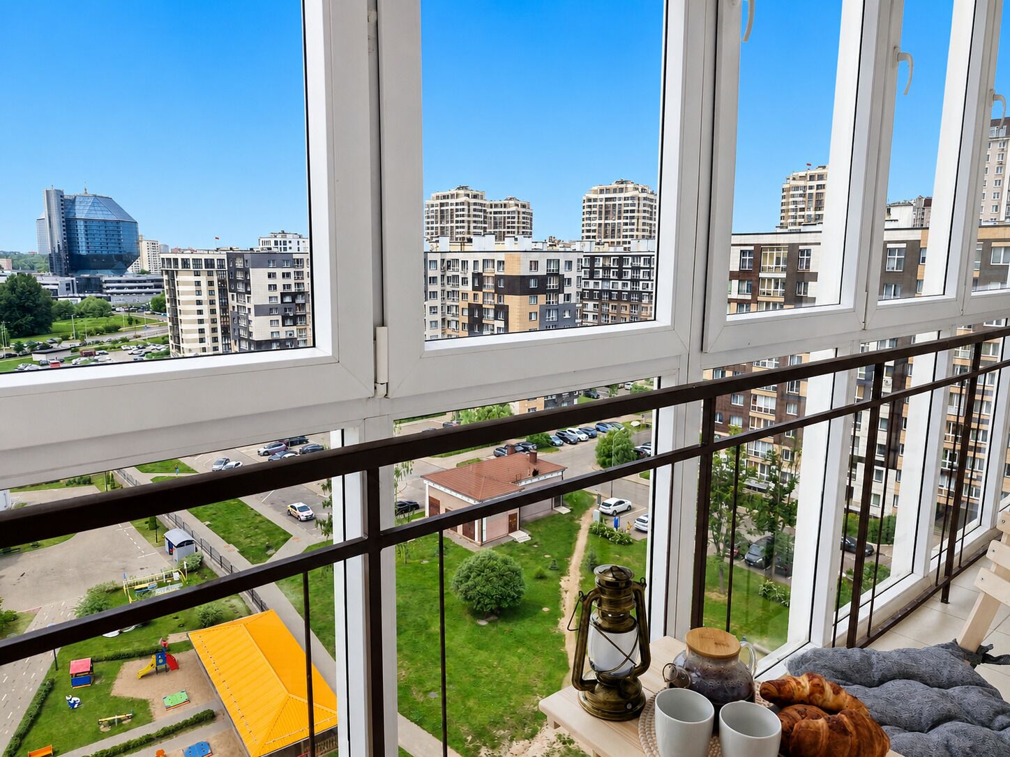 Un apartamento en un edificio alto con ventanas amplias que ofrece vistas de un paisaje urbano y un parque infantil más abajo.