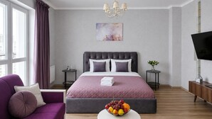 A modern bedroom with a large bed, a sofa, a small table with fruit, a TV, and a painting on the wall. - Modern Apartment with Library View (Minsk)