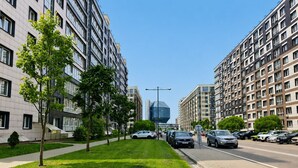 A modern urban street with high-rise residential buildings, a clear sky, and a well-maintained grassy median. - Modern Apartment with Library View (Minsk)