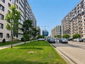 Una calle urbana moderna con edificios residenciales altos, cielo despejado y un césped cuidado en el centro.